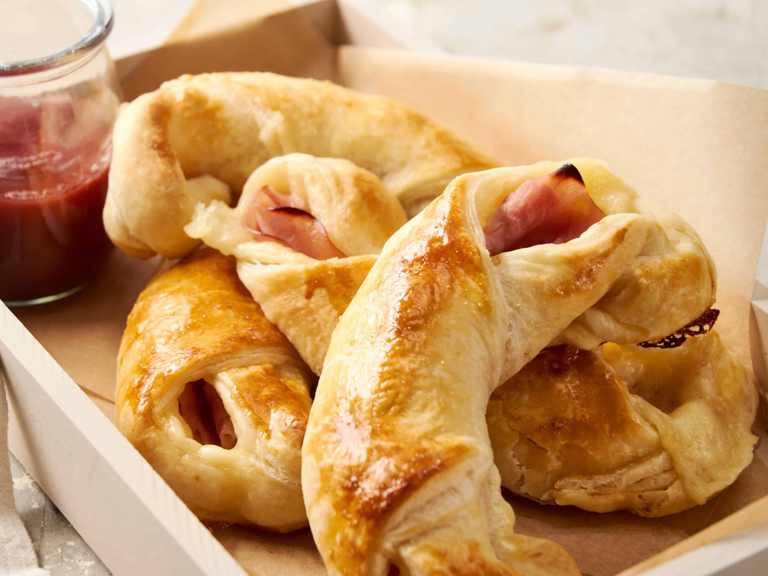 Golden baked ham and cheese croissants with flaky crust on a baking tray, served with a side of berry jam, perfect for breakfast or brunch.