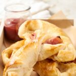 Buttered croissants with ham and cheese on a baking tray, perfect for breakfast or brunch, served with a side of jam in a glass jar for a delicious homemade meal.