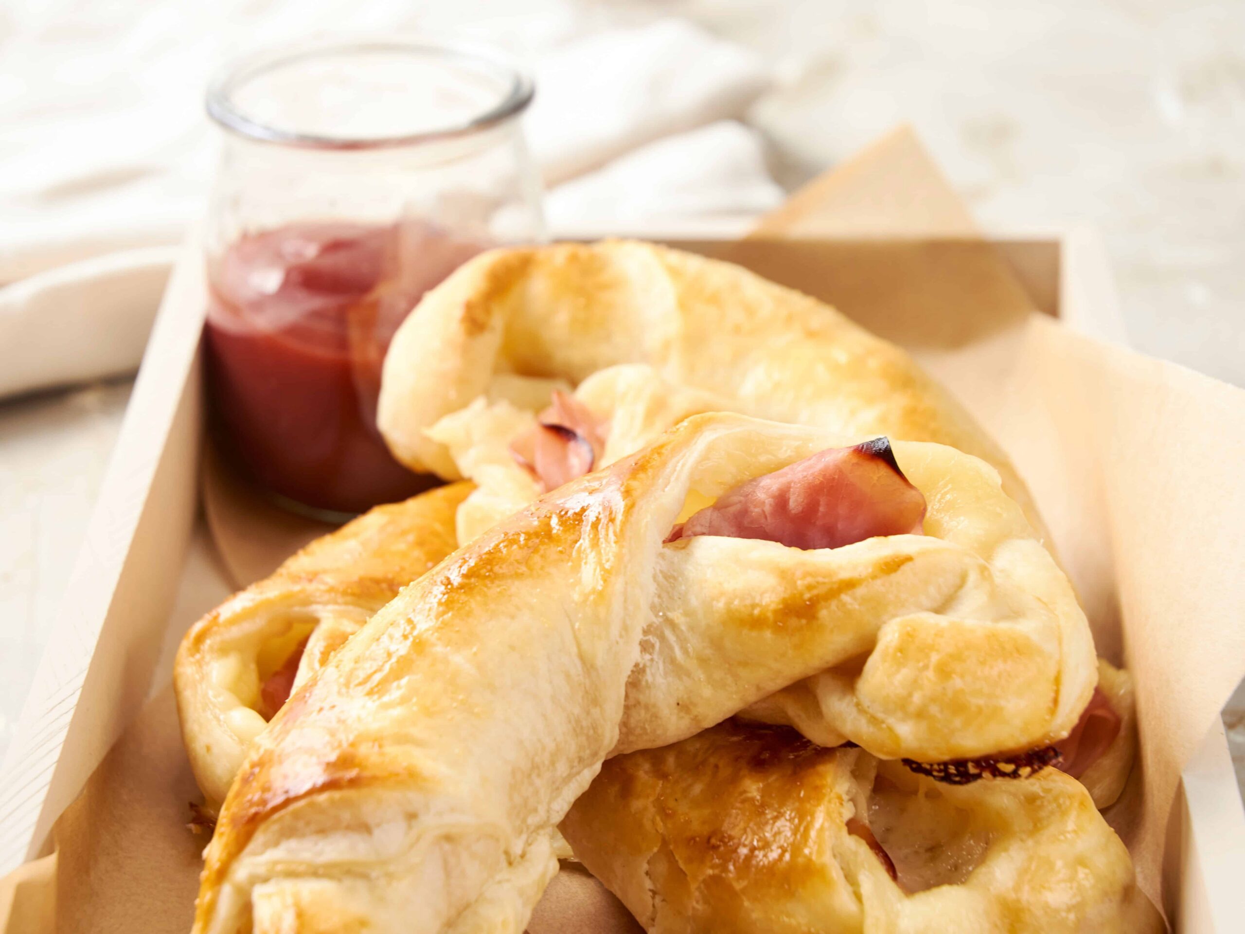 Buttered croissants with ham and cheese on a baking tray, perfect for breakfast or brunch, served with a side of jam in a glass jar for a delicious homemade meal.