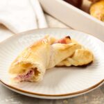Crunchy ham and cheese stuffed croissant baked to golden perfection on a white plate, perfect for breakfast or snack.