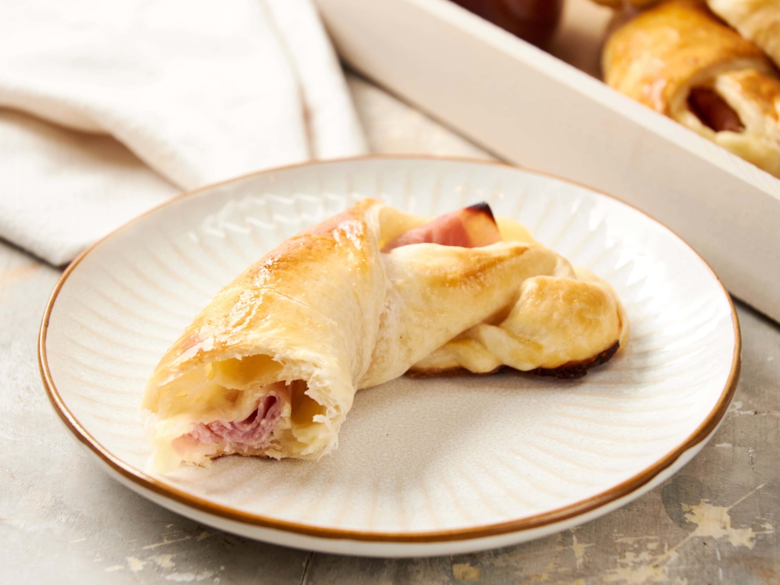Crunchy ham and cheese stuffed croissant baked to golden perfection on a white plate, perfect for breakfast or snack.