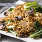 Sauteed chicken and vegetable stir-fry with noodles, mushrooms, and fresh greens on a white plate, served with soy sauce. Perfect for quick, healthy Asian-inspired meals.