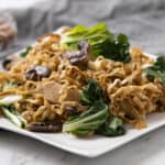 Stir-fried noodles with chicken, mushrooms, and bok choy on a white plate, healthy Asian-inspired dish for lunch or dinner.