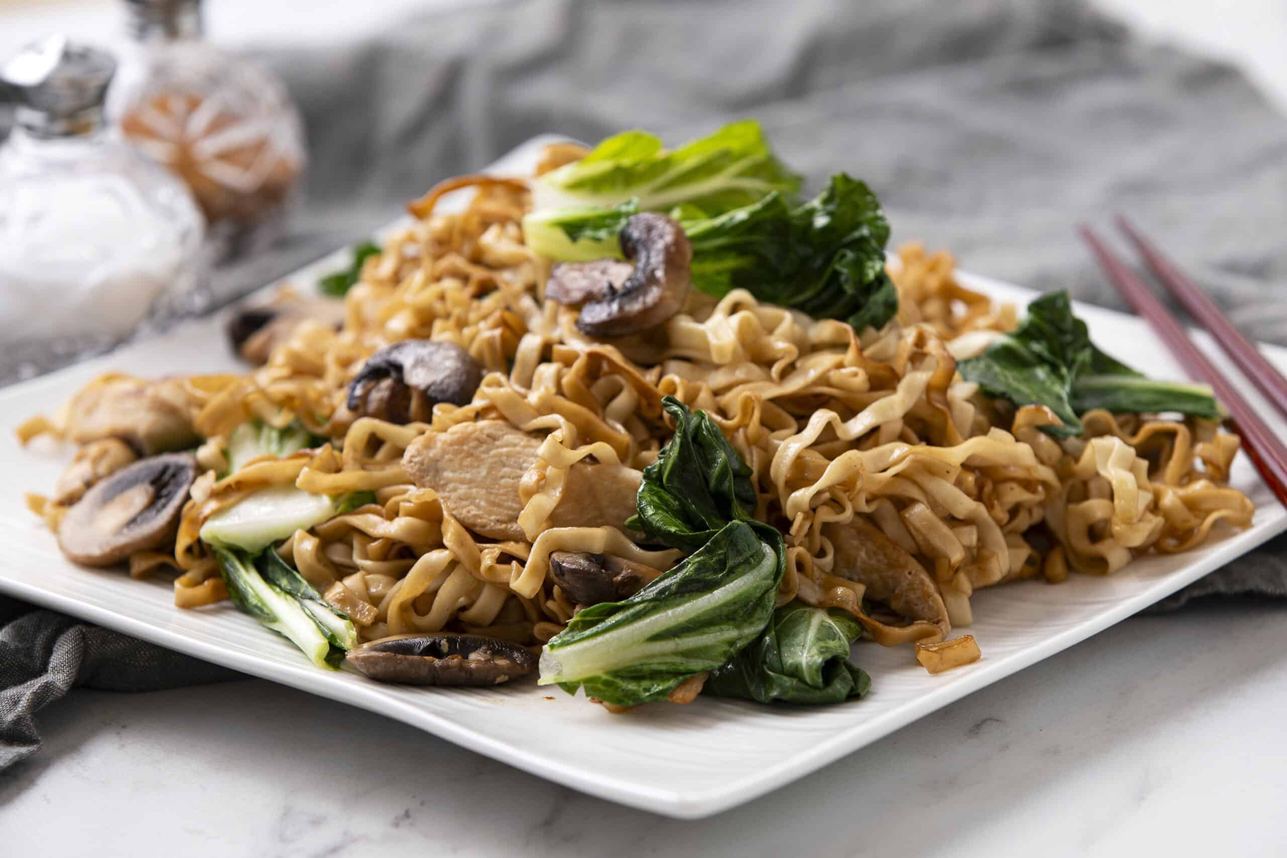 Stir-fried noodles with chicken, mushrooms, and bok choy on a white plate, healthy Asian-inspired dish for lunch or dinner.