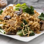 Stir-fried noodles with vegetables and mushrooms on a white rectangular plate, featuring bok choy and sliced chicken for a healthy Asian-inspired dish.