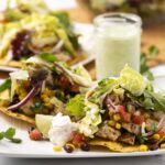 Crispy fish tacos with fresh vegetables, avocado, and lime on a white plate with cilantro garnish and side sauce, delicious healthy seafood recipe, best taco ideas.