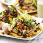 Fresh chicken taco with lettuce, tomatoes, black beans, corn, and salsa on a white plate with cilantro garnish.