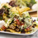 Fresh taco salad with grilled chicken, mixed greens, corn, black beans, tomatoes, and creamy avocado dressing, topped with crispy tortilla chips on a white plate.