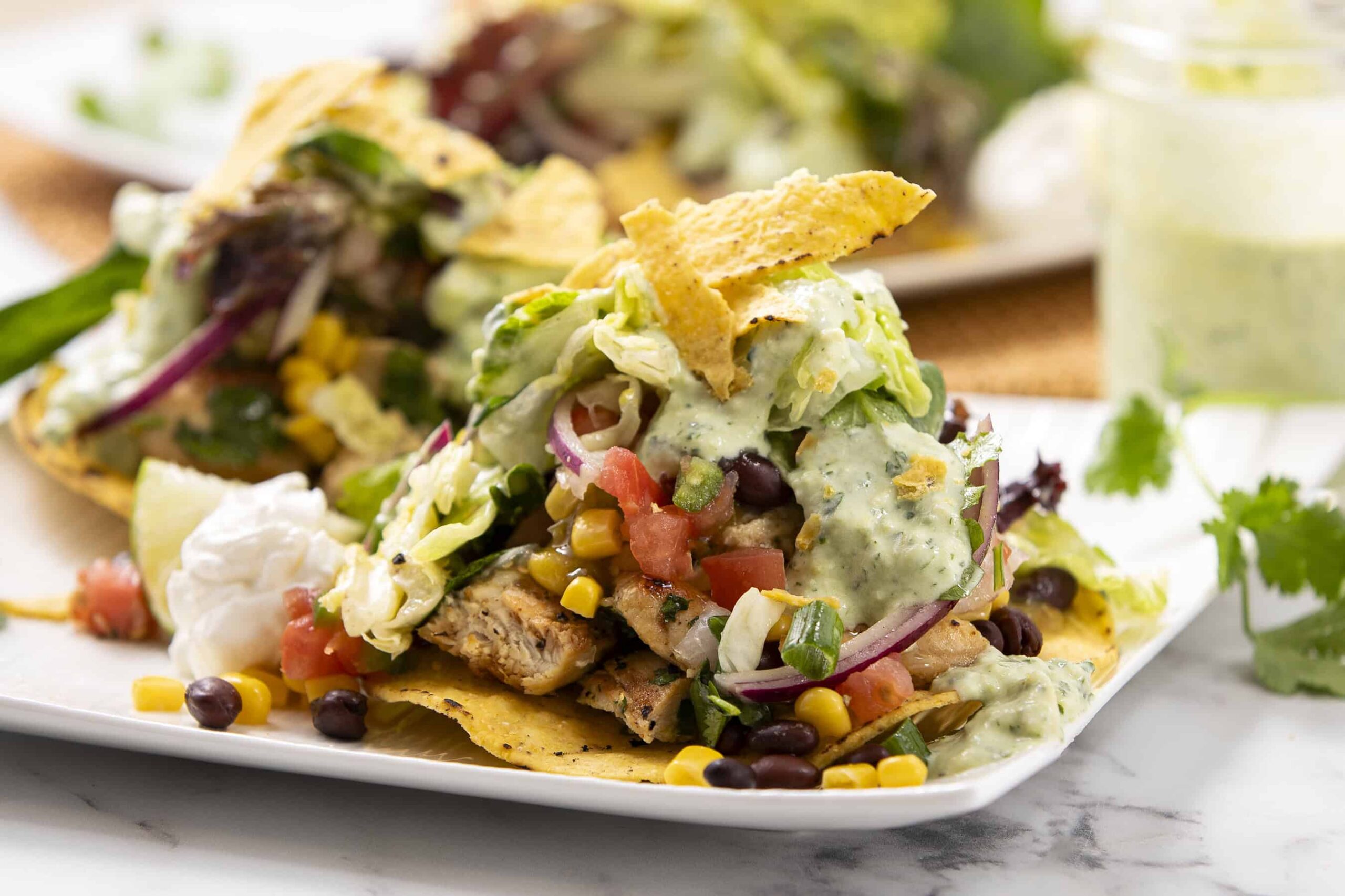 Fresh taco salad with grilled chicken, mixed greens, corn, black beans, tomatoes, and creamy avocado dressing, topped with crispy tortilla chips on a white plate.