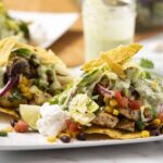 Fresh chicken fajitas with colorful vegetables, creamy guacamole, sour cream, and crispy tortilla chips served on a white plate. Perfect for a delicious Mexican-inspired meal.