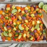 Roasted chicken and colorful vegetable sheet tray dinner with pineapple chunks, lime wedges, and cilantro garnish on a baking sheet.