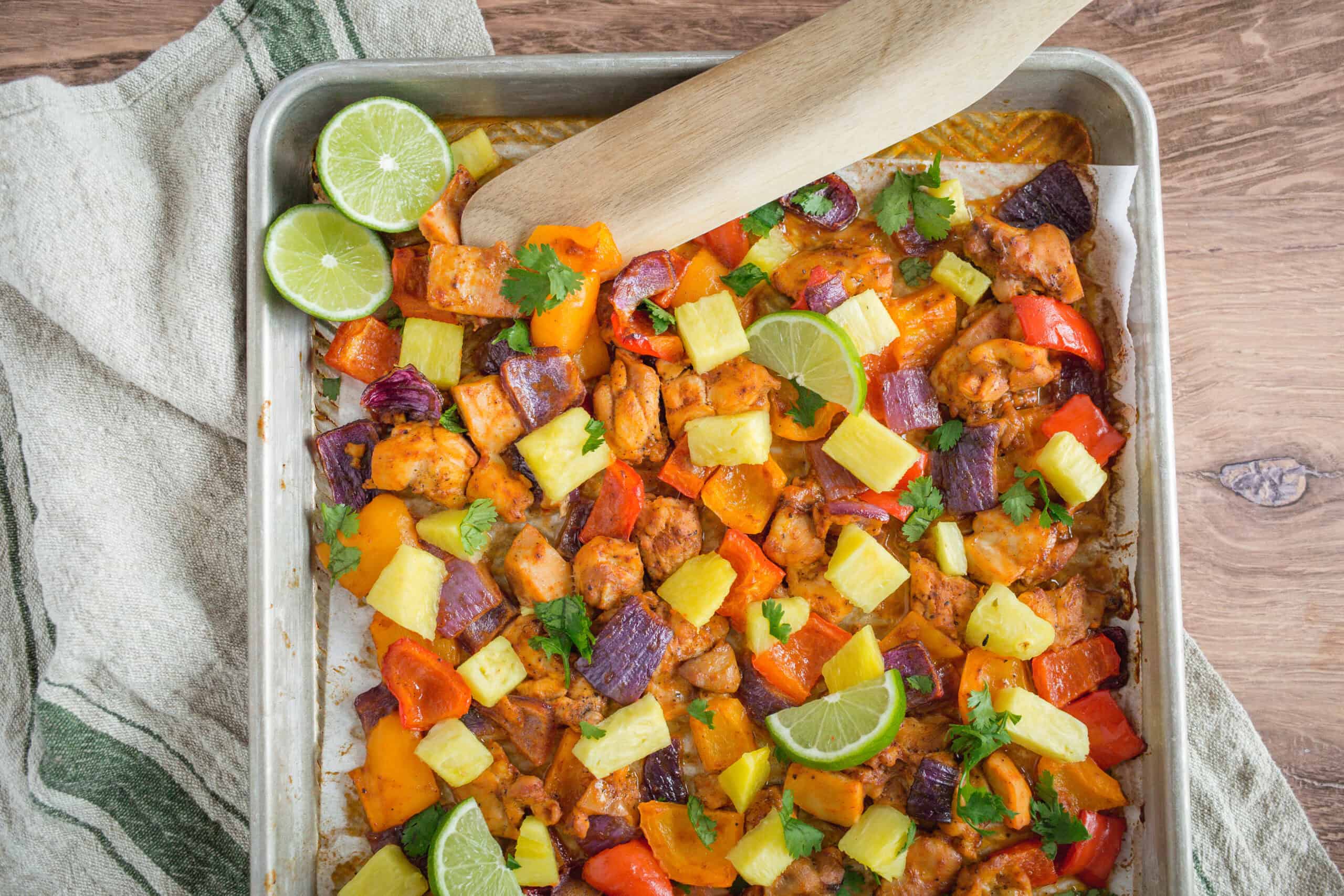 Sautéed chicken and mixed vegetables in a flavorful sauce topped with pineapple chunks, lime wedges, and fresh cilantro on a baking sheet. Perfect for quick, healthy meal recipes and delicious flavorful dinners.