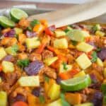 Freshly cooked chicken fajitas with colorful bell peppers, pineapple chunks, lime wedges, and cilantro on a baking sheet, perfect for a tasty Mexican-inspired meal.