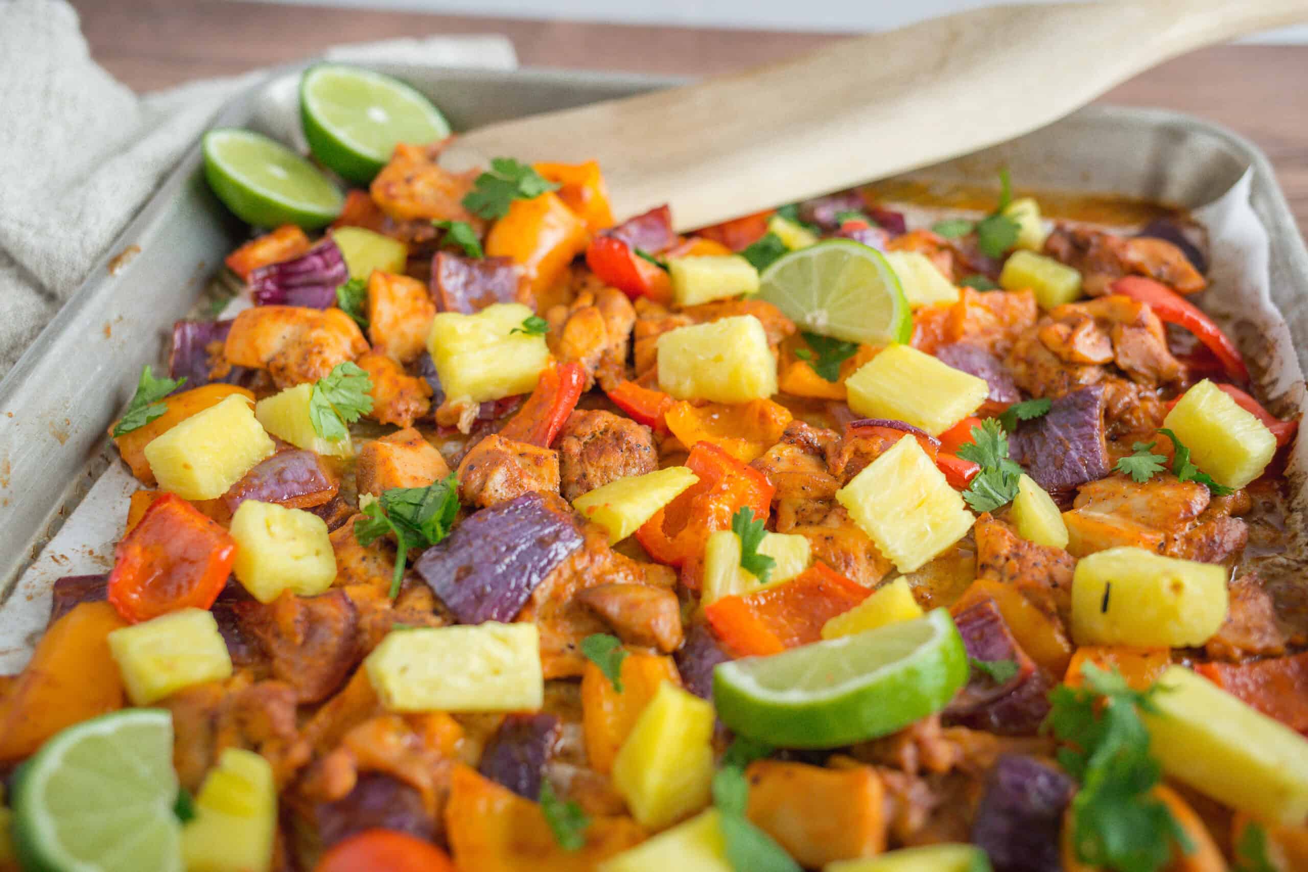 Freshly cooked chicken fajitas with colorful bell peppers, pineapple chunks, lime wedges, and cilantro on a baking sheet, perfect for a tasty Mexican-inspired meal.