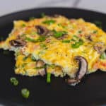 Fluffy mushroom and vegetable omelette garnished with chopped green onions on a black plate. Perfect for breakfast, brunch, or any meal, this delicious dish combines eggs, fresh vegetables, and savory mushrooms.