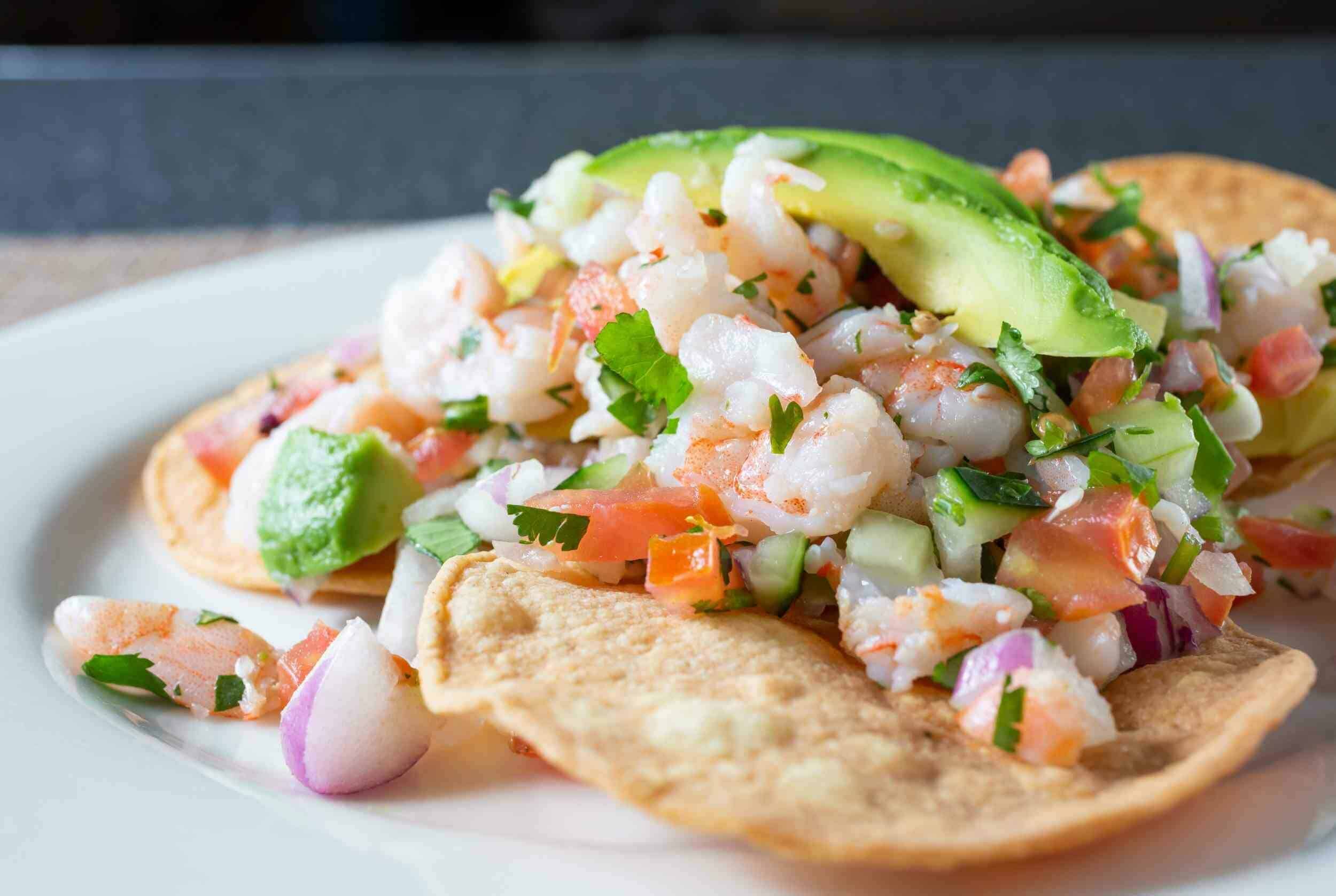 Fresh seafood ceviche on a crispy taco shell with avocado, tomatoes, onions, and herbs, served on a white plate, showcasing vibrant colors and fresh ingredients, perfect for seafood and Mexican cuisine lovers.