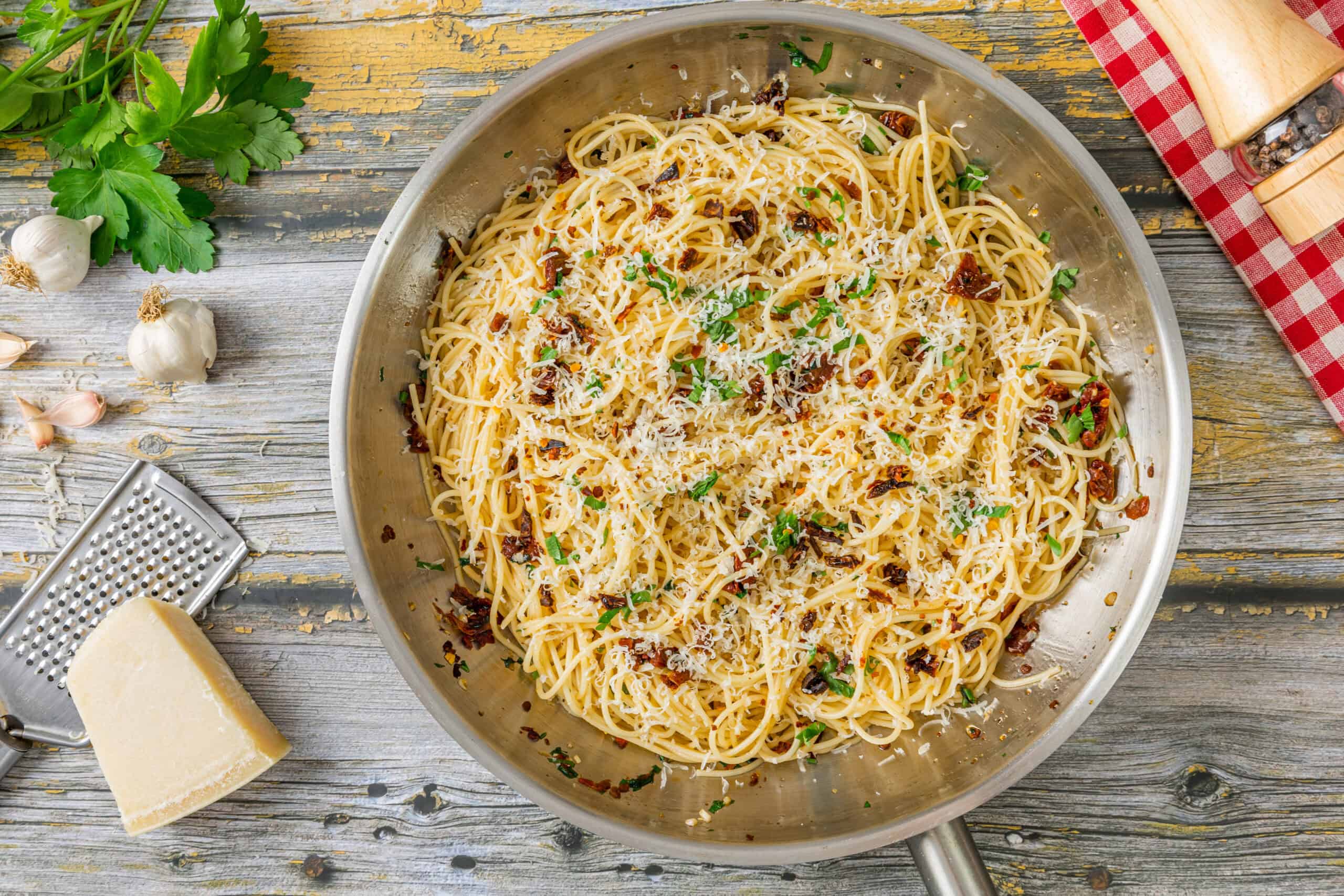 Creamy garlic Parmesan pasta with sun-dried tomatoes and fresh herbs in a stainless steel skillet on rustic wooden table. Perfect for easy, flavorful Italian dinner recipes.