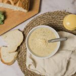 Creamy broccoli cheese soup served with shredded cheese, fresh broccoli florets, and sliced bread on a rustic woven placemat. Perfect for comfort food recipes and quick homemade soup ideas.