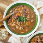 Hearty beans and vegetable soup served in a green-rimmed bowl with rustic bread and fresh herbs, perfect for a comforting meal or homemade dinner recipe.