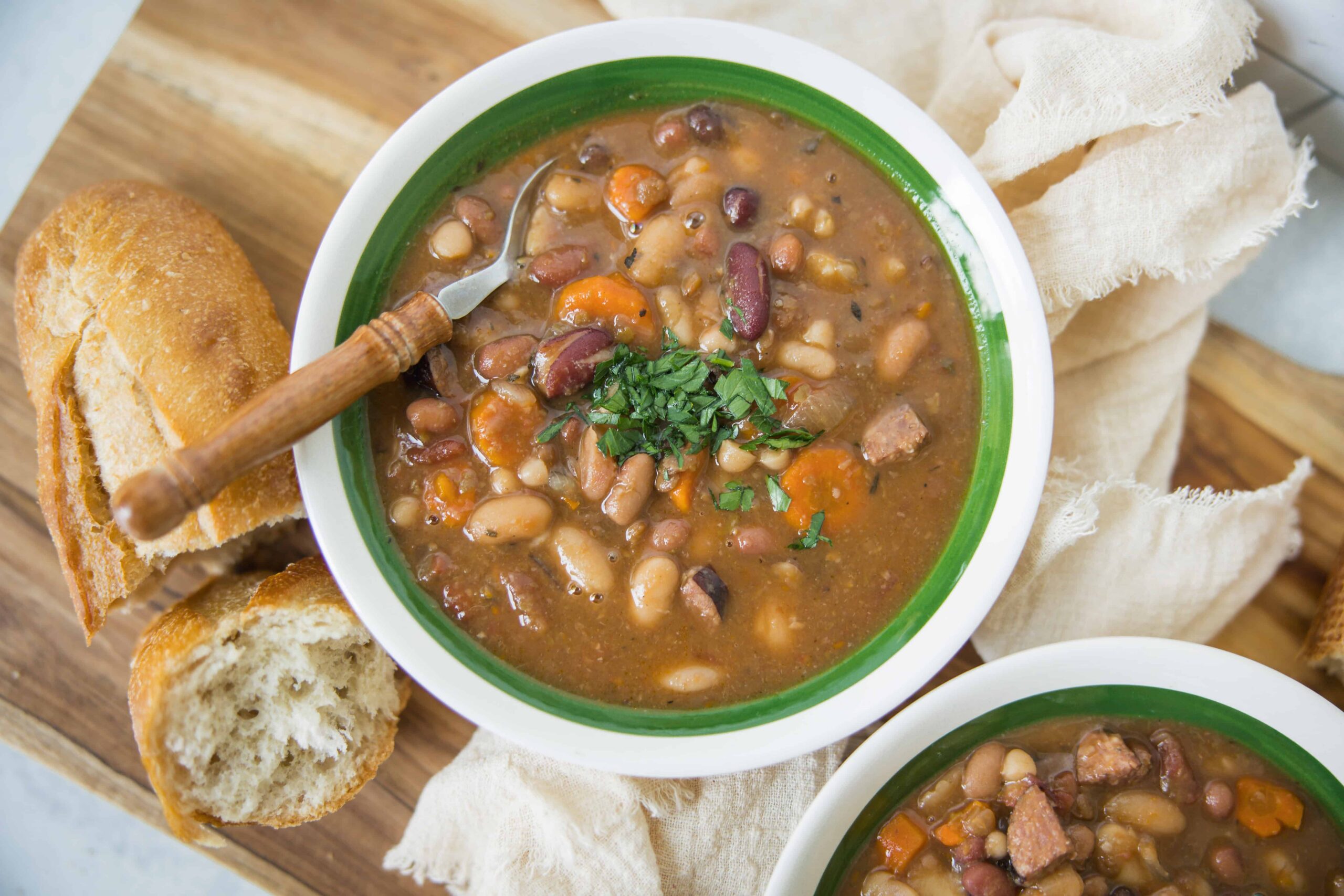 Hearty beans and vegetable soup served in a green-rimmed bowl with rustic bread and fresh herbs, perfect for a comforting meal or homemade dinner recipe.