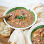 2. Hearty bean and meat chili served in a green-rimmed bowl with fresh herbs, accompanied by bread on a wooden tray, perfect for comforting meals and family dinners.