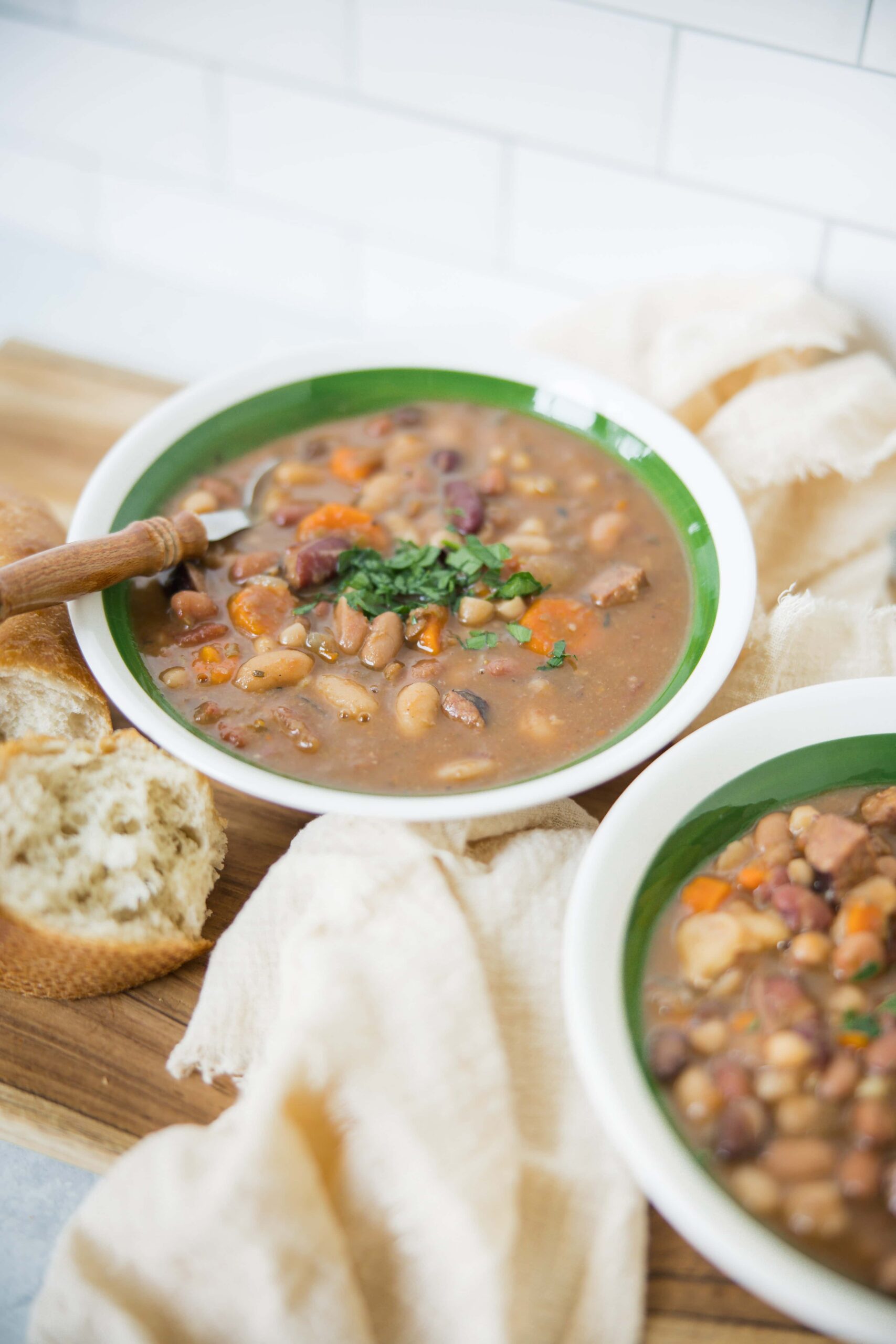 2. Hearty bean and meat chili served in a green-rimmed bowl with fresh herbs, accompanied by bread on a wooden tray, perfect for comforting meals and family dinners.