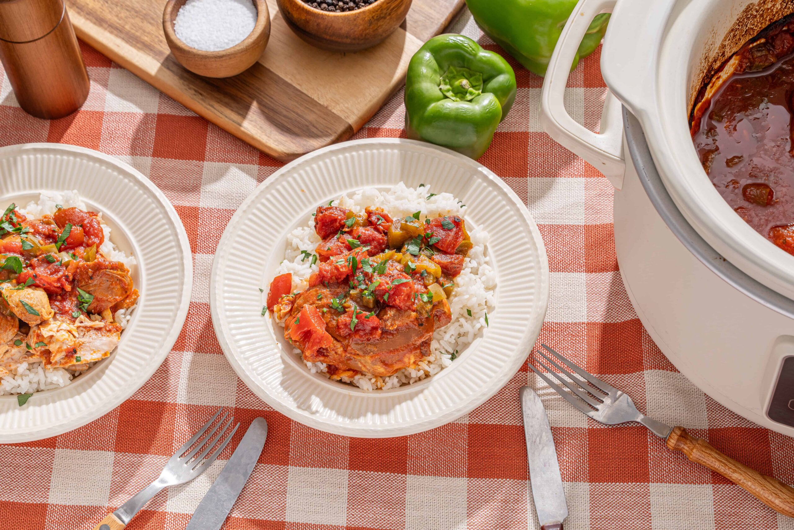 Savory stew served over rice on a plate with fresh green bell peppers and ingredients in the background.
