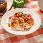 Cooked chicken and vegetable stir-fry served over white rice on a beige plate.