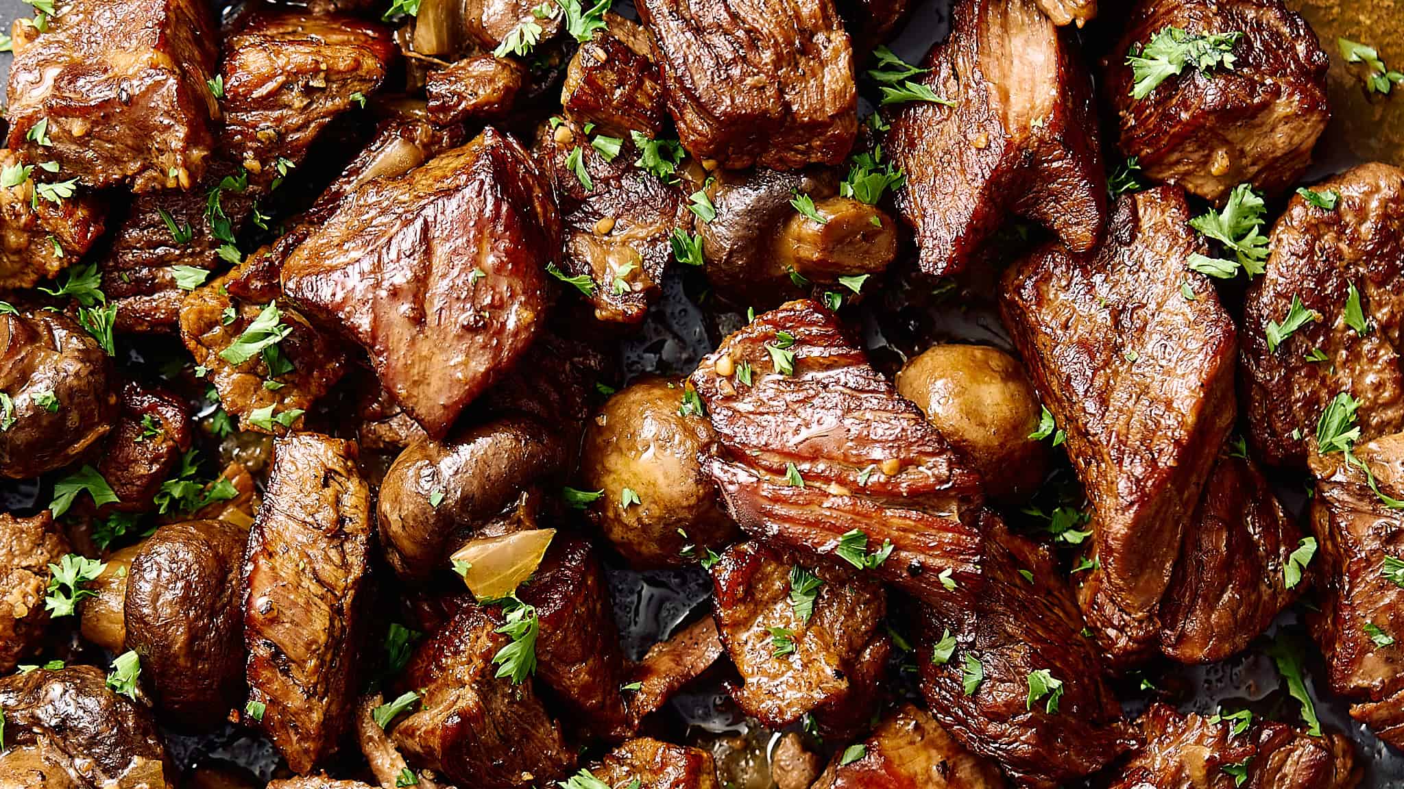 Tender beef stew meat cooked to perfection with mushrooms and herbs, garnished with fresh parsley for a flavorful, savory meal.