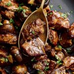 Braised beef stew with mushrooms and herbs in a dark skillet.
