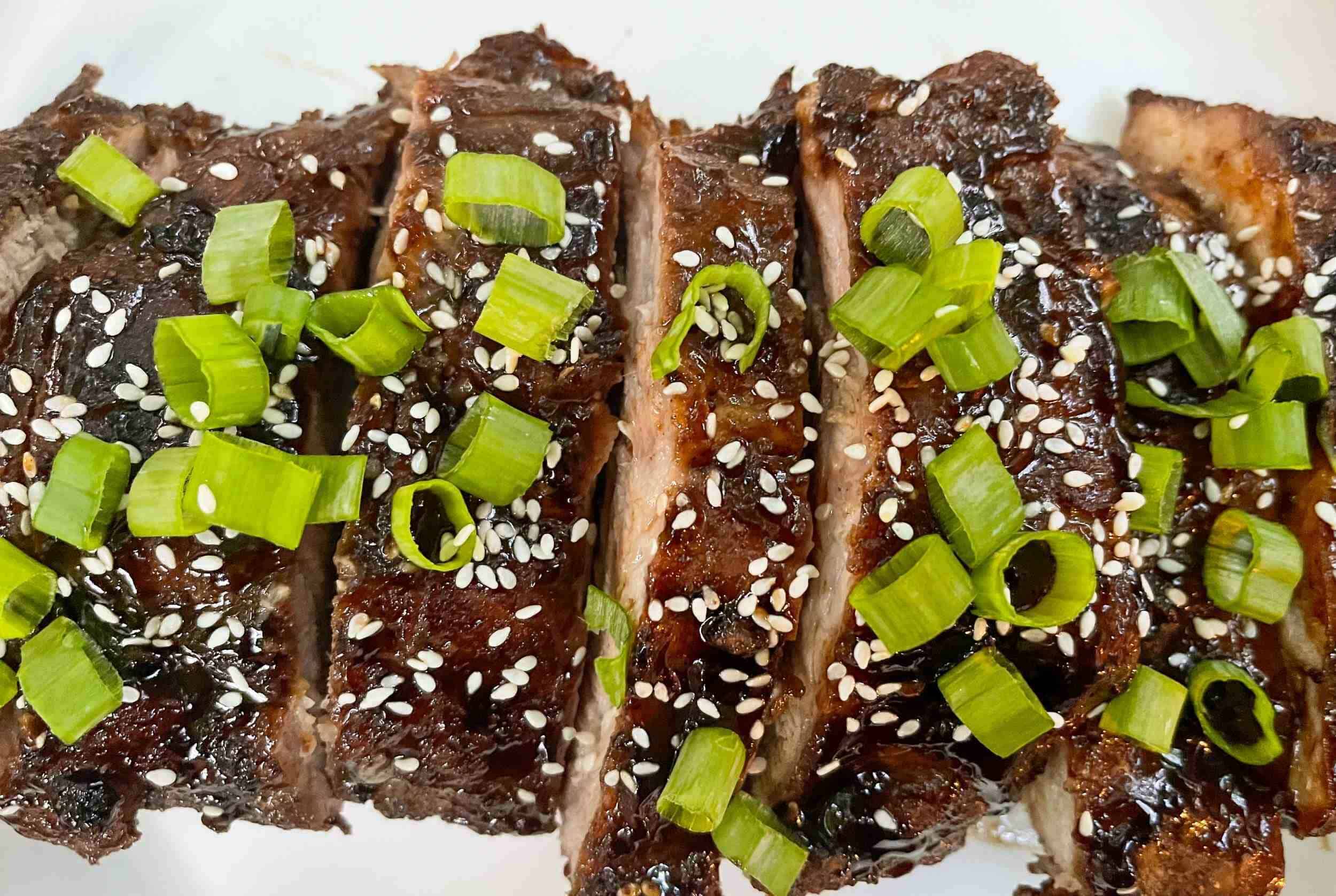 Succulent BBQ pork ribs topped with chopped green onions, sesame seeds, and a glossy sauce, served on a white plate for a flavorful and appealing dish of Asian-inspired cuisine.