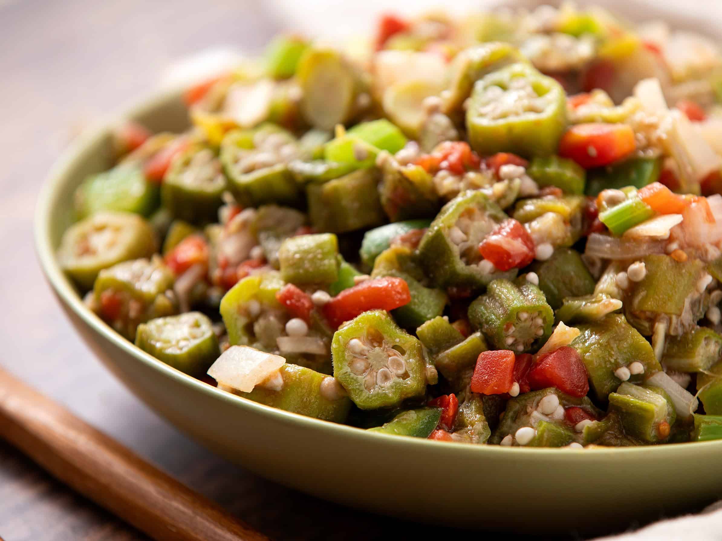 Sautéed okra with diced tomatoes, onions, and green onions in a bowl on a wooden surface, showcasing a healthy and flavorful vegetable dish.