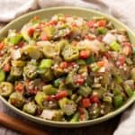 Freshly cooked okra mixed with diced tomatoes, onions, and peppers in a green bowl, ready to serve as a flavorful vegetable side dish or healthy meal option.