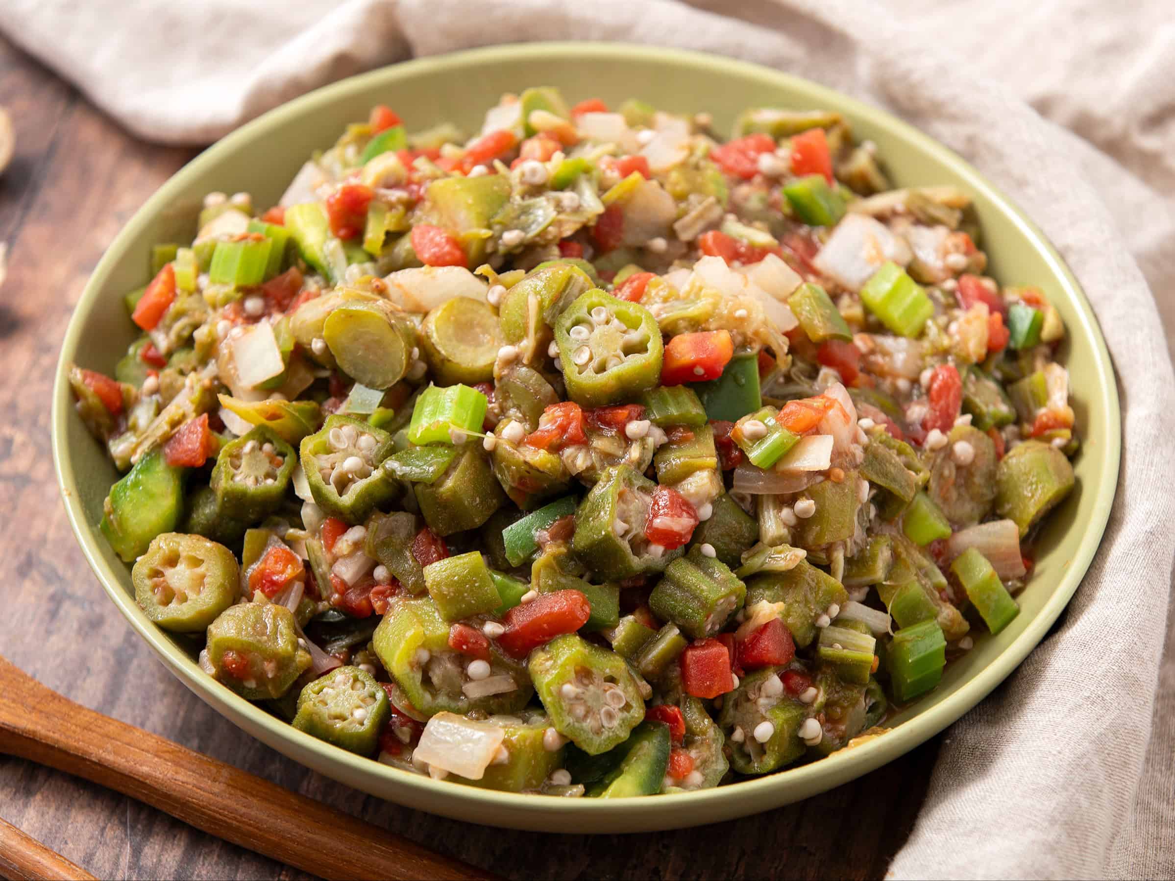 Freshly cooked okra mixed with diced tomatoes, onions, and peppers in a green bowl, ready to serve as a flavorful vegetable side dish or healthy meal option.