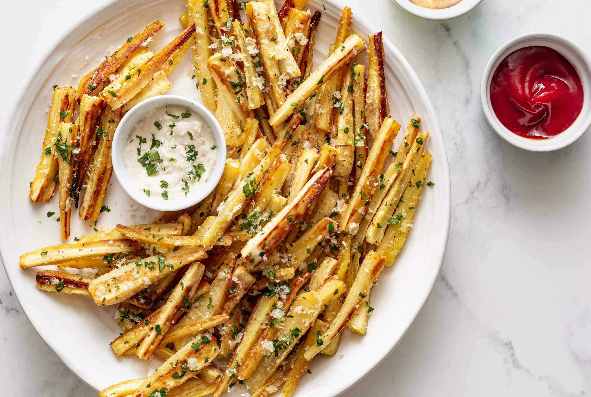 Crispy oven-baked potato fries with parsley and grated cheese on white plate with dipping sauces.