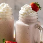 Creamy strawberry milkshake topped with whipped cream and fresh strawberries, served in a mason jar for a refreshing dessert or snack. Perfect for summer or special occasions.