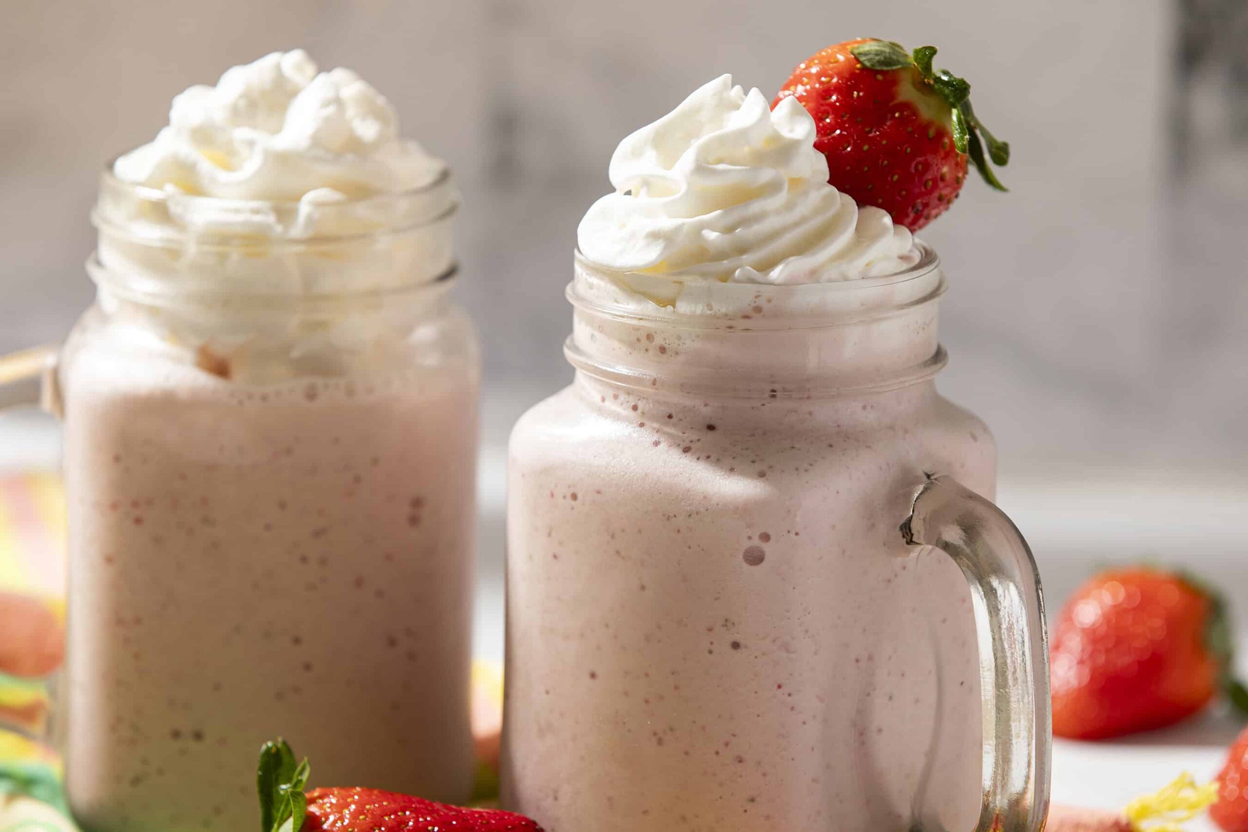 Creamy strawberry milkshake topped with whipped cream and fresh strawberries, served in a mason jar for a refreshing dessert or snack. Perfect for summer or special occasions.