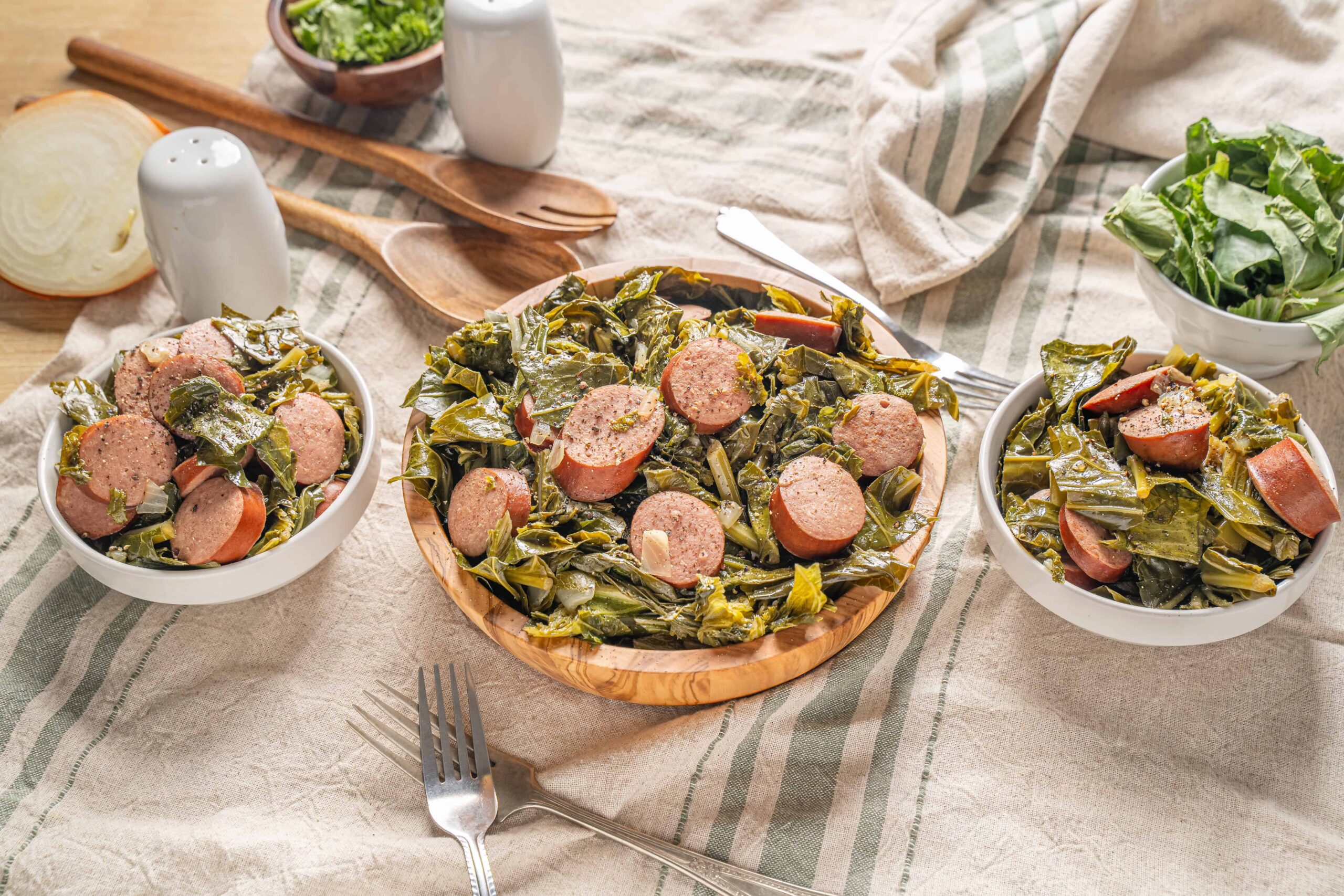 Savory sausage and collard greens on a rustic wooden table, served in white bowls and a wooden plate, ready for a delicious homemade meal with fresh ingredients and comforting flavors.