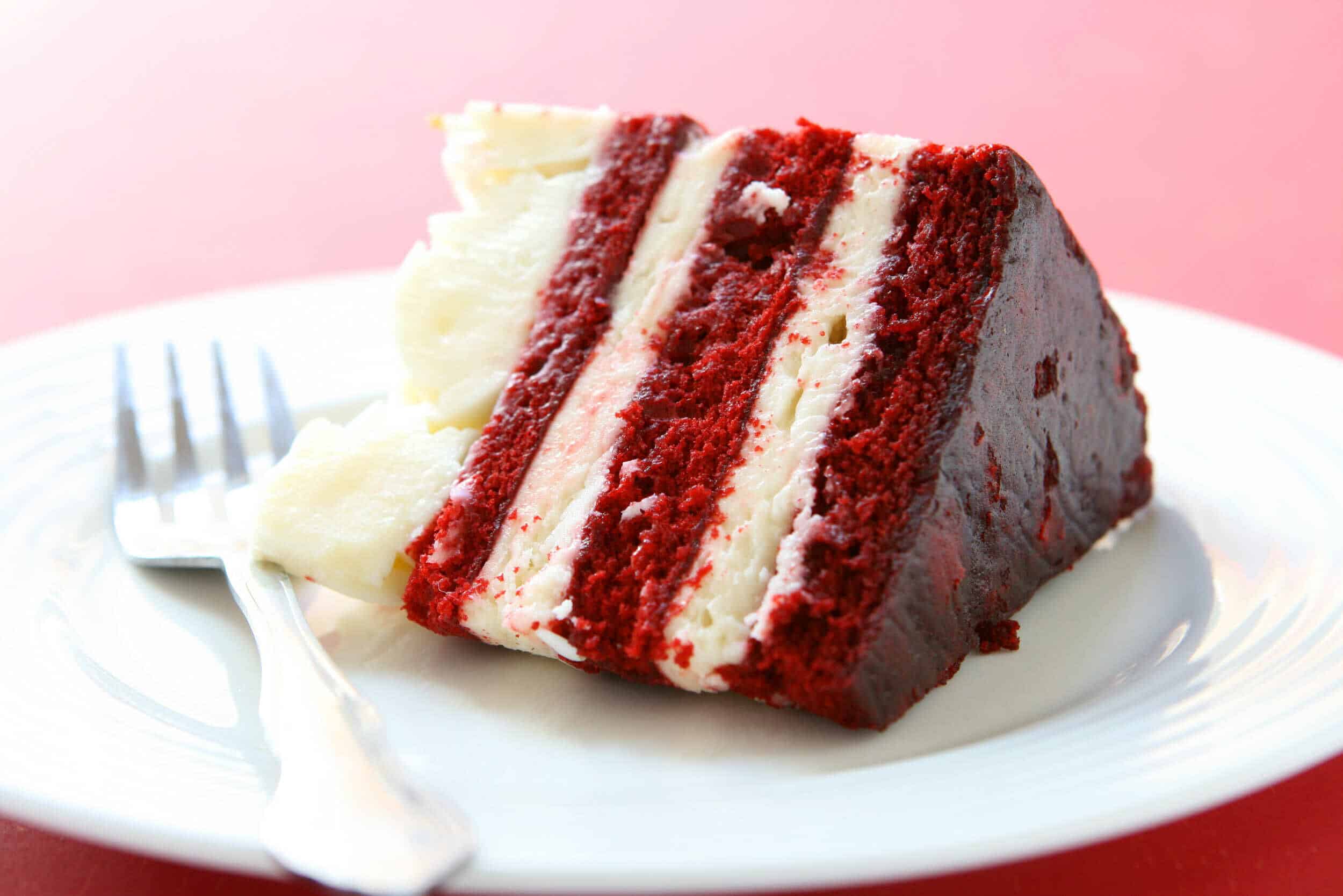 Red velvet cake with cream cheese frosting, sliced on white plate with fork, soft texture, rich red color, layered dessert, perfect for celebrations and special occasions.