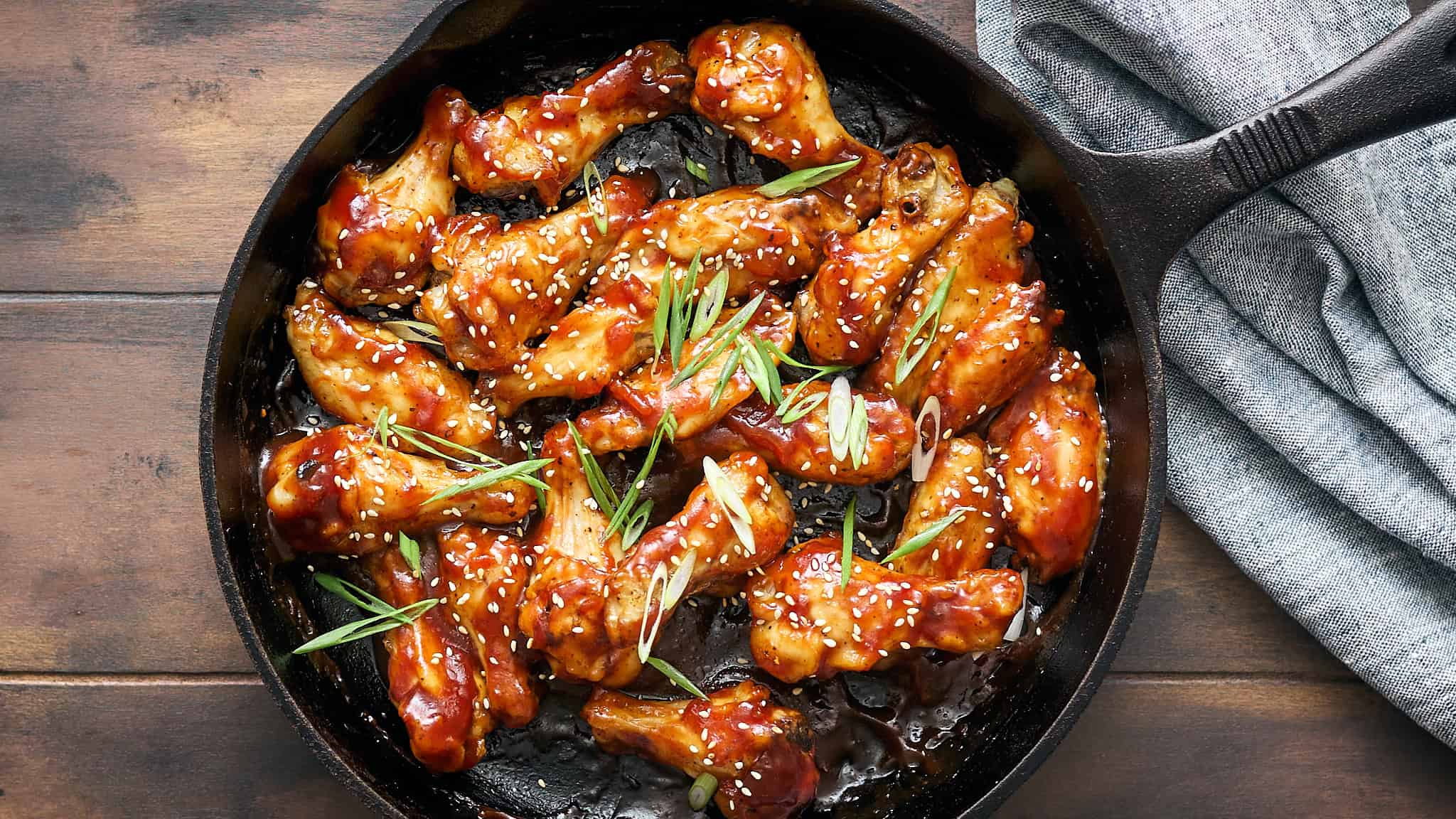 Crispy buffalo chicken wings in black cast iron skillet garnished with green onions and sesame seeds on wooden table.