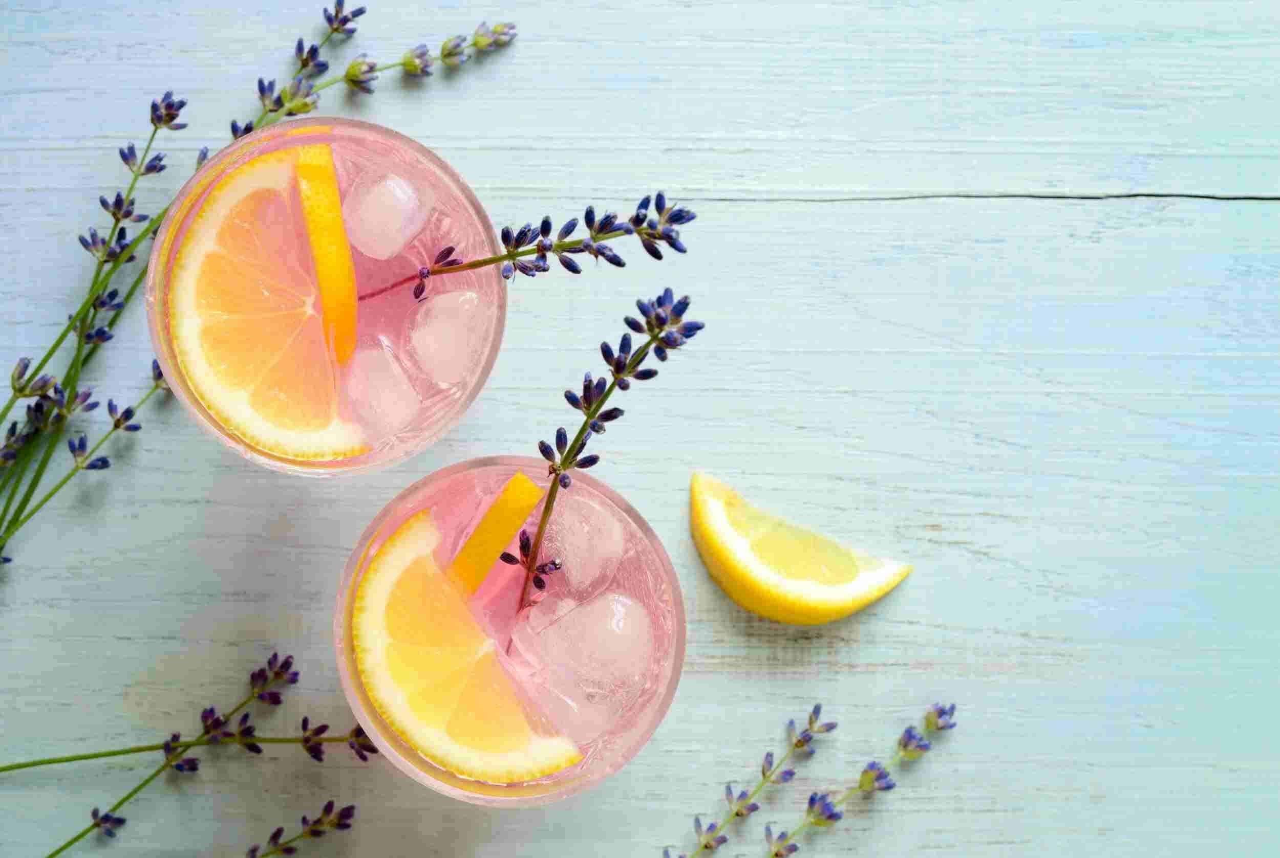 Rose lemonade with lemon slices and lavender sprigs on a light wooden surface, refreshing summer drink, floral infused beverage, cold pink lemonade, aesthetic beverage presentation.