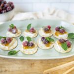 Fresh cranberry and brie cheese canapé appetizers garnished with mint leaves on a light green plate, perfect for festive parties and holiday gatherings.