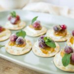 Mini cheese and fruit canapé appetizers with fresh berries, mint leaves, and honey on crackers, perfect for appetizer recipes and party snacks.