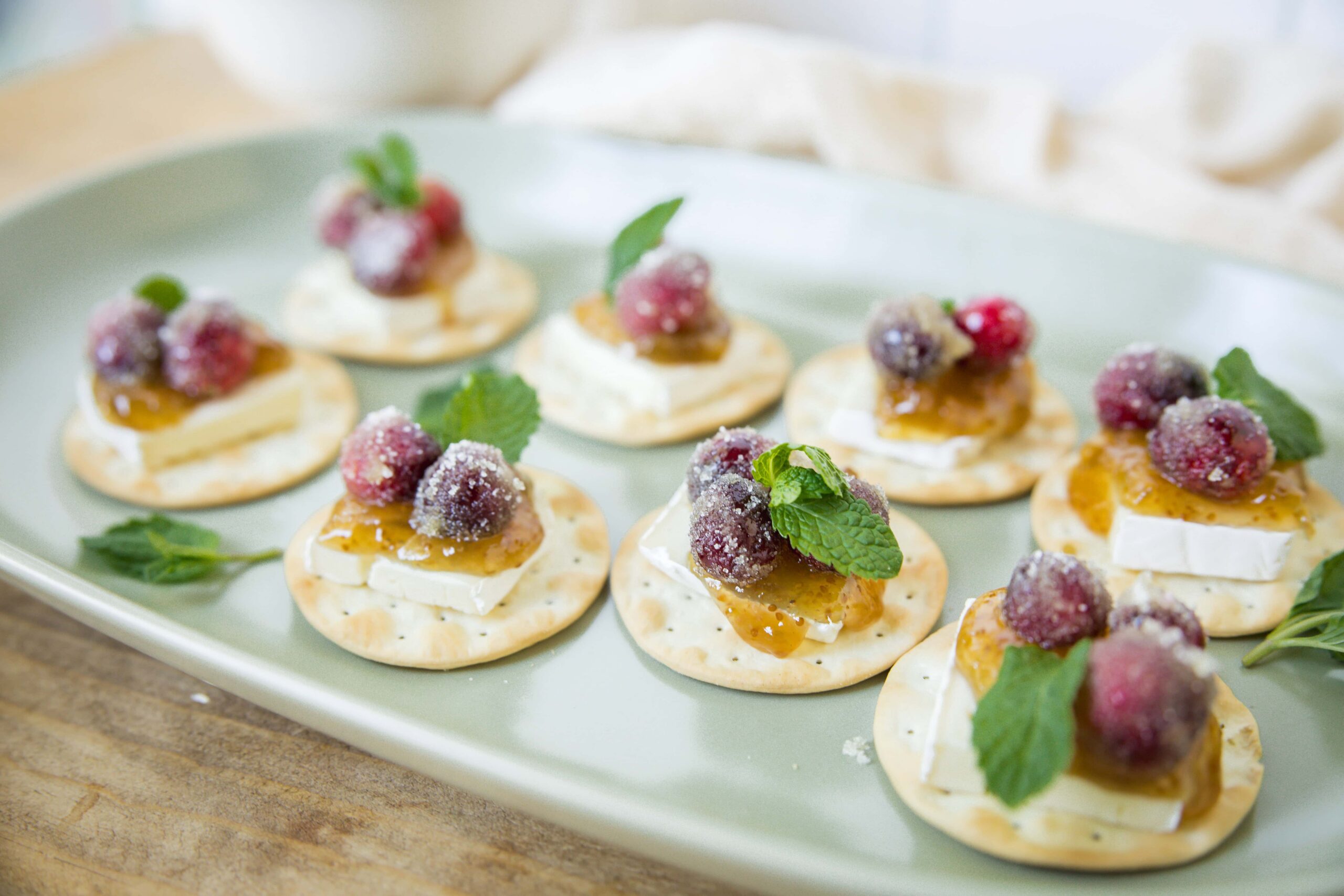 Mini cheese and fruit canapé appetizers with fresh berries, mint leaves, and honey on crackers, perfect for appetizer recipes and party snacks.