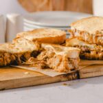 Creamy pulled pork sandwich with melted cheese on toasted bread, served on a wooden cutting board. Perfect comfort food for lunch or dinner, featuring savory flavors and melty cheese.