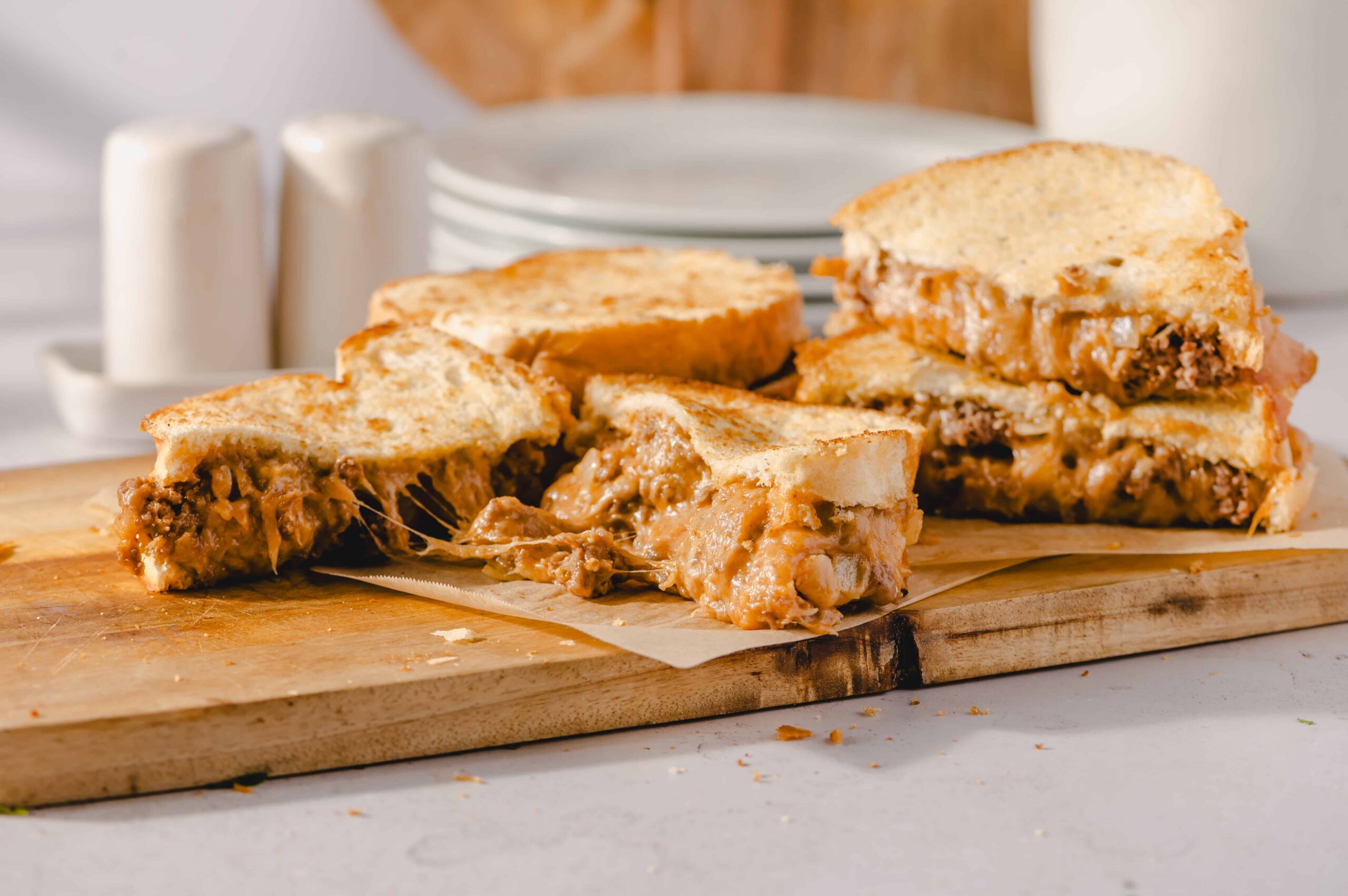 Creamy pulled pork sandwich with melted cheese on toasted bread, served on a wooden cutting board. Perfect comfort food for lunch or dinner, featuring savory flavors and melty cheese.