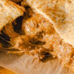 Creamy peanut butter and jelly sandwich with melted cheese oozing out, close-up of a gooey grilled cheese sandwich filled with peanut butter and jelly, delicious comfort food with crispy bread and melting cheese.