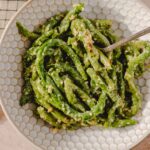 Crispy green beans salad with garlic and red pepper flakes in a white patterned bowl on a textured surface.
