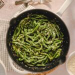 Freshly cooked green bean pasta with grated cheese in a skillet, topped with garlic and herbs, on a light-colored kitchen countertop. Perfect for a healthy, tasty meal or side dish for dinner.