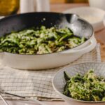 Freshly cooked green beans with garlic and seasonings, served in a white bowl with a fork, on a wooden table for a healthy and flavorful vegetable dish.